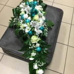 Egy fekete kofferen a földön egy széles csokor, fehér virágokkal és kék díszekkel.