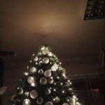Egy karácsonyfa fehér díszekkel és fényekkel egy sötét teremben.
