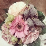 Egy csokor nagy zöld levelekkel, rózsaszín és lila virágokkal.