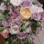 Egy kéz lila, fehér és narancs rózsákat tart.