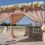 Egy magas teraszon, összeadó pavilonnal, rózsaszín függönnyel.