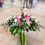 A homokszínű járólapon, fehér és rózsaszín virágok csokorba szedve egy magasabb átlátszó vázában.