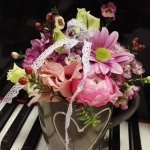 Zongora billentyűin, szürke bögre, rózsaszín és sárga virágokkal.