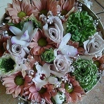 Kör alakú virágtartóban zöld, fehér és rózsaszínű virágok.