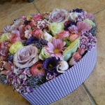 Egy szív alakú virágtartóban sárga, piros, lila, rózsaszín és kék virágok.