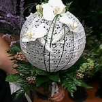 Egy kér fog egy fehér, gömb alakú dekorációt, három fehér virággal az oldalán.