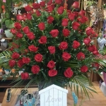 Egy vázában hosszú zöld szárú vörös rózsa csokor.